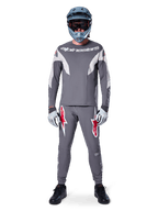 MTB-rytter iført Alpinestars A-Supra Race bukser i mørkegrå, med markante røde logo-detaljer på lårene, matchende grå jersey, blå full-face hjelm og sorte sko, komplet off-road racersæt