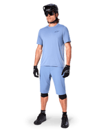 Model iført Alpinestars A-Dura shorts i Infinity Blue, matchende lyseblå kortærmet jersey, sort MTB-hjelm, solbriller og sorte handsker, komplet mountainbike-outfit til trail-kørsel