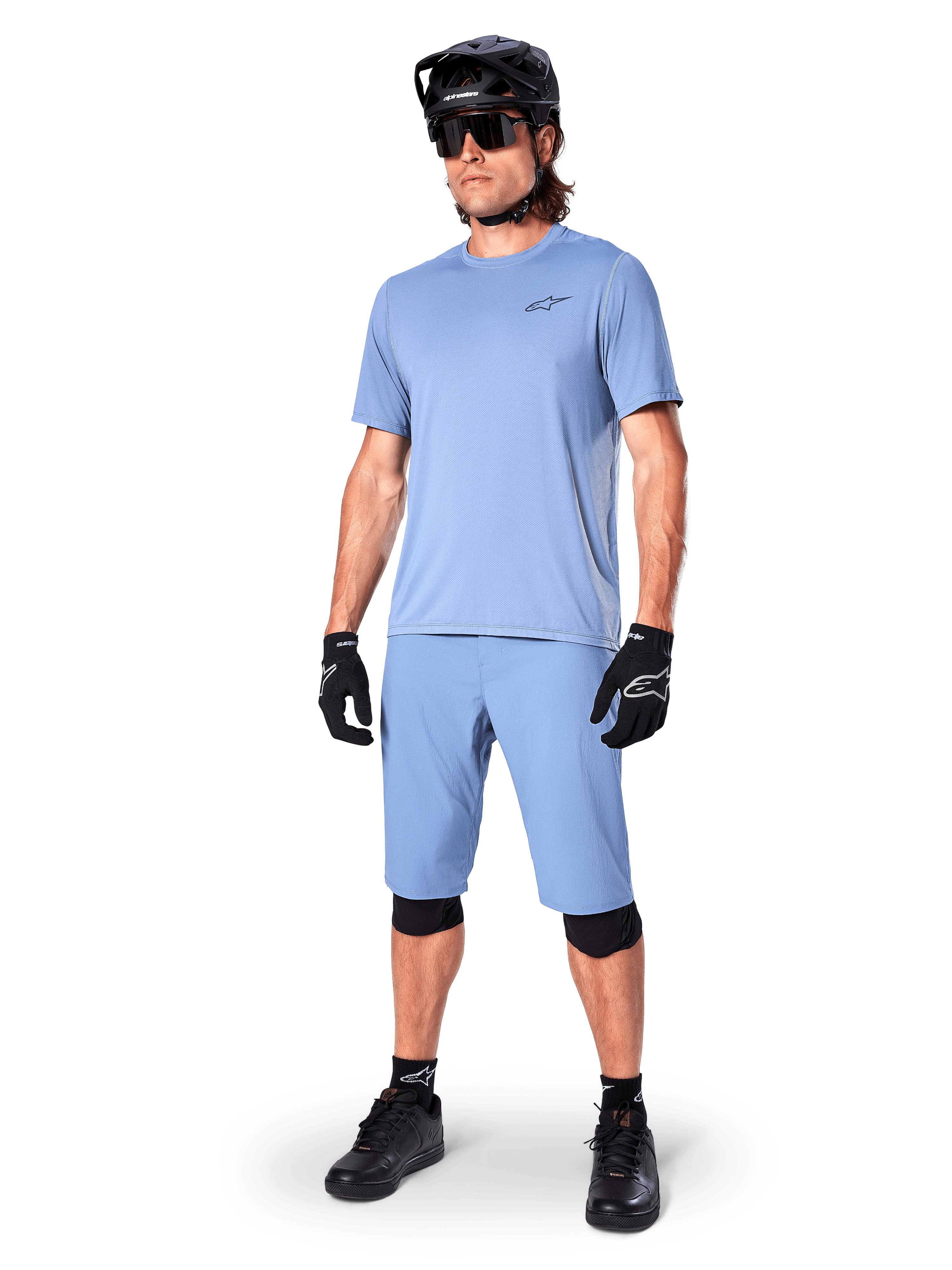 Model iført Alpinestars A-Dura shorts i Infinity Blue, matchende lyseblå kortærmet jersey, sort MTB-hjelm, solbriller og sorte handsker, komplet mountainbike-outfit til trail-kørsel