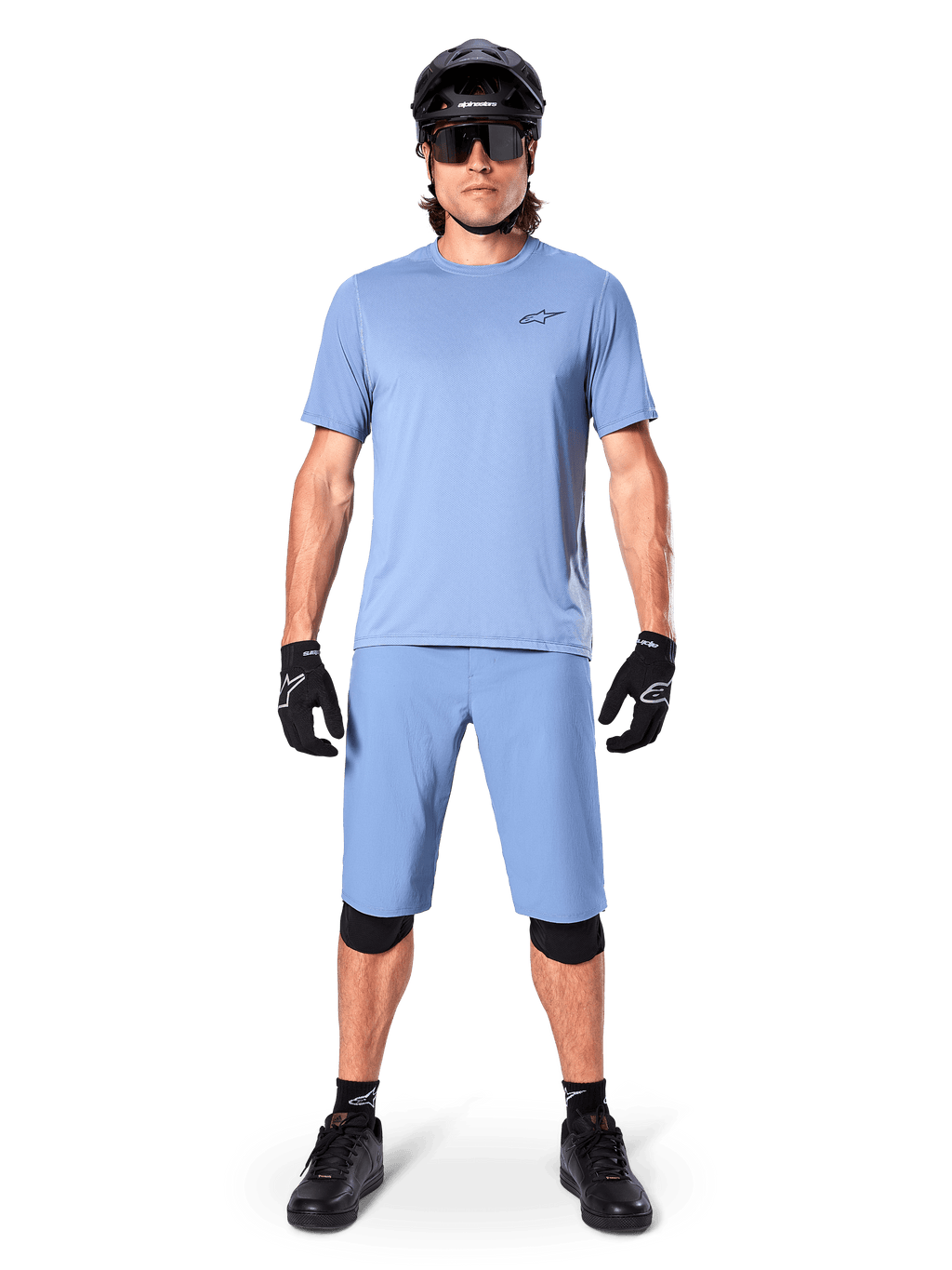 Model iført Alpinestars A-Dura shorts i Infinity Blue, matchende lyseblå jersey, sort mountainbikehjelm, sorte solbriller, sorte handsker og knæbeskyttere, komplet MTB-outfit til trailkørsel