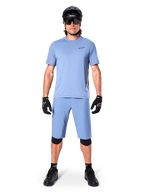 Model iført Alpinestars A-Dura shorts i Infinity Blue, matchende lyseblå jersey, sort mountainbikehjelm, sorte solbriller, sorte handsker og knæbeskyttere, komplet MTB-outfit til trailkørsel