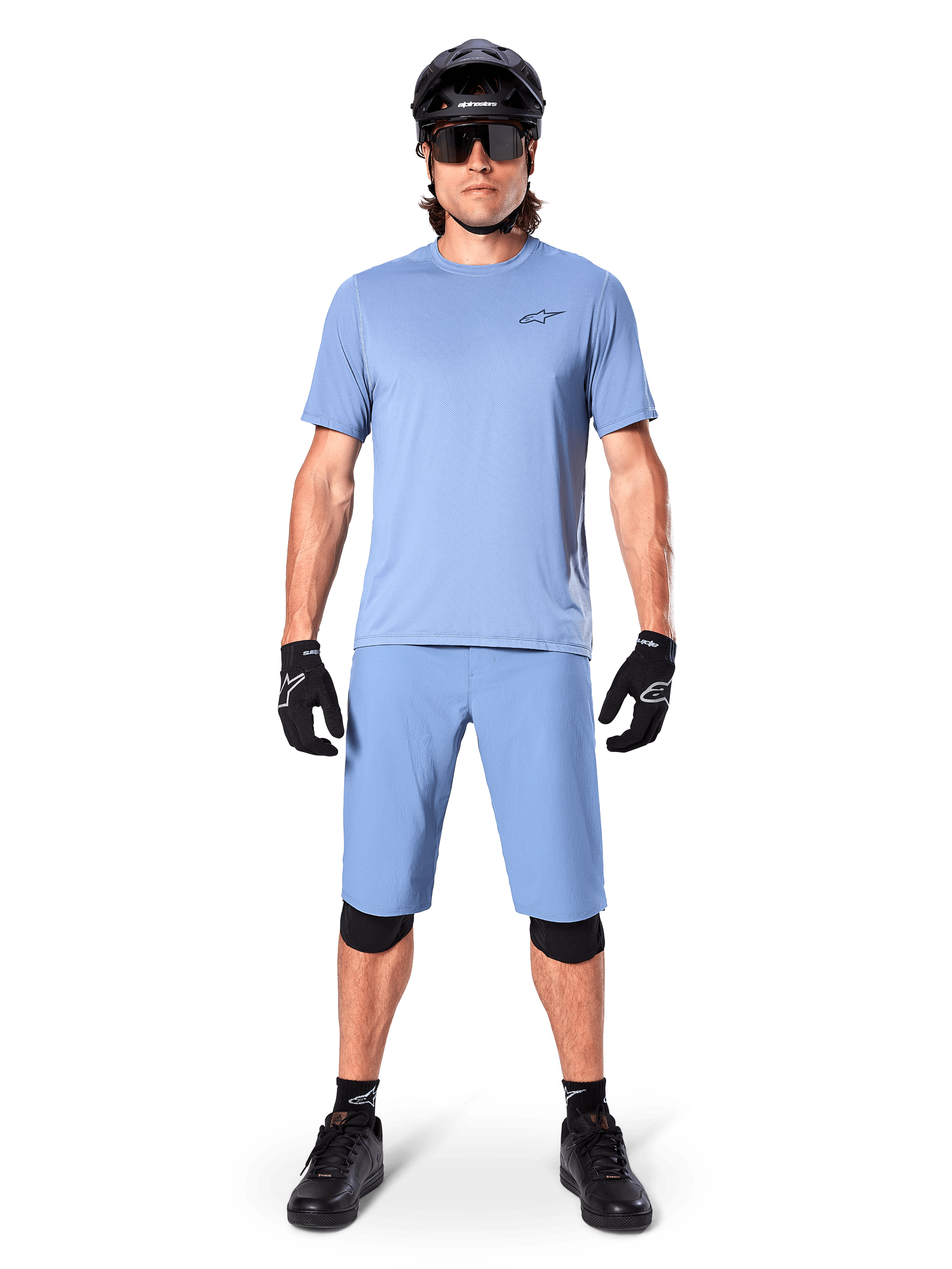 Model iført Alpinestars A-Dura shorts i Infinity Blue, matchende lyseblå jersey, sort mountainbikehjelm, sorte solbriller, sorte handsker og knæbeskyttere, komplet MTB-outfit til trailkørsel