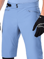 Alpinestars A-Dura Shorts, Infinity Blue mountainbike-shorts, nærbillede af taljen med dobbelt snaplukning, justerbar sidejustering og lynlåslommer med mesh-foring, båret med en sort Alpinestars-handske