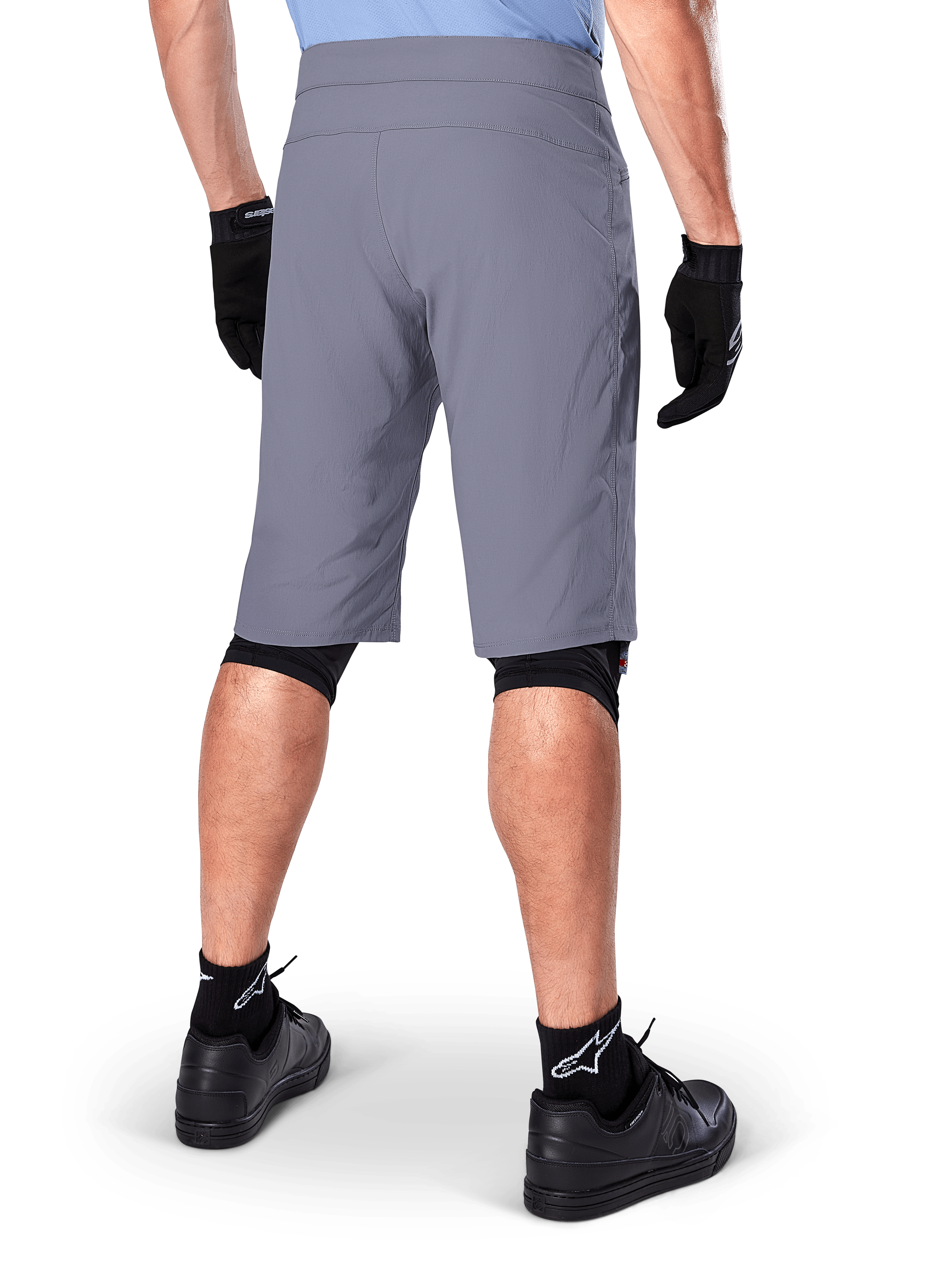 Alpinestars A-Dura Shorts, mørkegrå mountainbike-shorts, set bagfra på en rytter, bæres med sorte handsker, sorte knæ-liners og sorte sokker med Alpinestars-logo, holdbar konstruktion til terrænkørsel