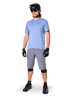 Alpinestars A-Dura shorts, MTB-shorts, mørkegrå, båret af en rytter med lyseblå trøje, sort MTB-hjelm, sorte handsker og knæbeskyttere, komplet mountainbike-outfit til trail- og terrænkørsel