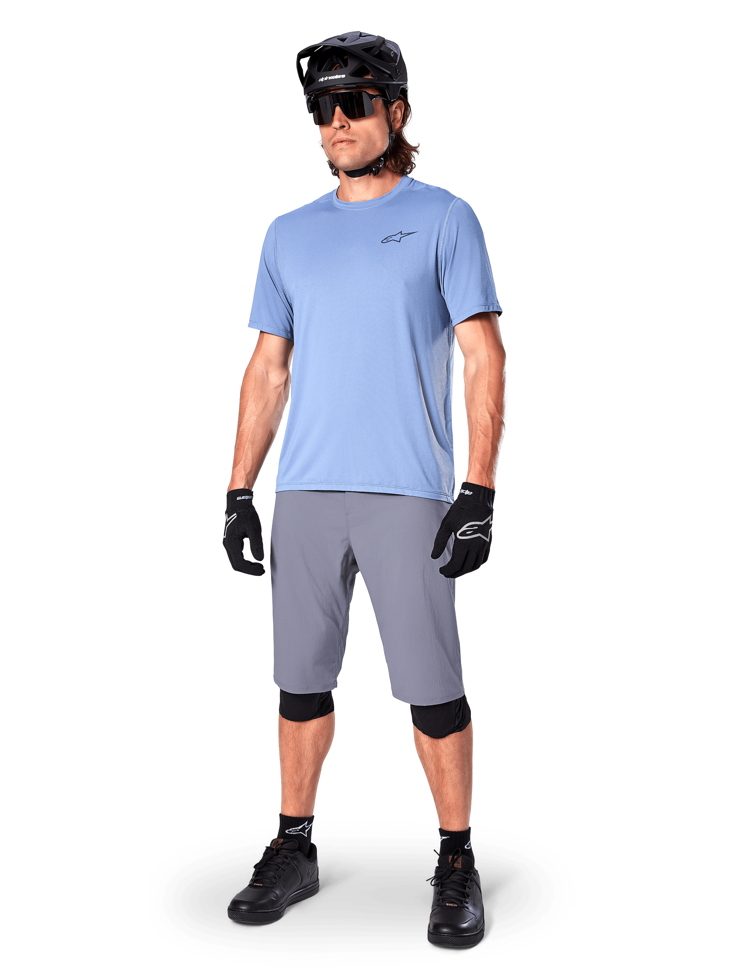 Alpinestars A-Dura shorts, MTB-shorts, mørkegrå, båret af en rytter med lyseblå trøje, sort MTB-hjelm, sorte handsker og knæbeskyttere, komplet mountainbike-outfit til trail- og terrænkørsel