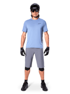 Mandlig rytter iført Alpinestars A-Dura Shorts i mørkegrå, kombineret med en lyseblå kortærmet t-shirt, sort hjelm, solbriller og sorte knæbeskyttere, komplet mountainbike-outfit til terrænkørsel