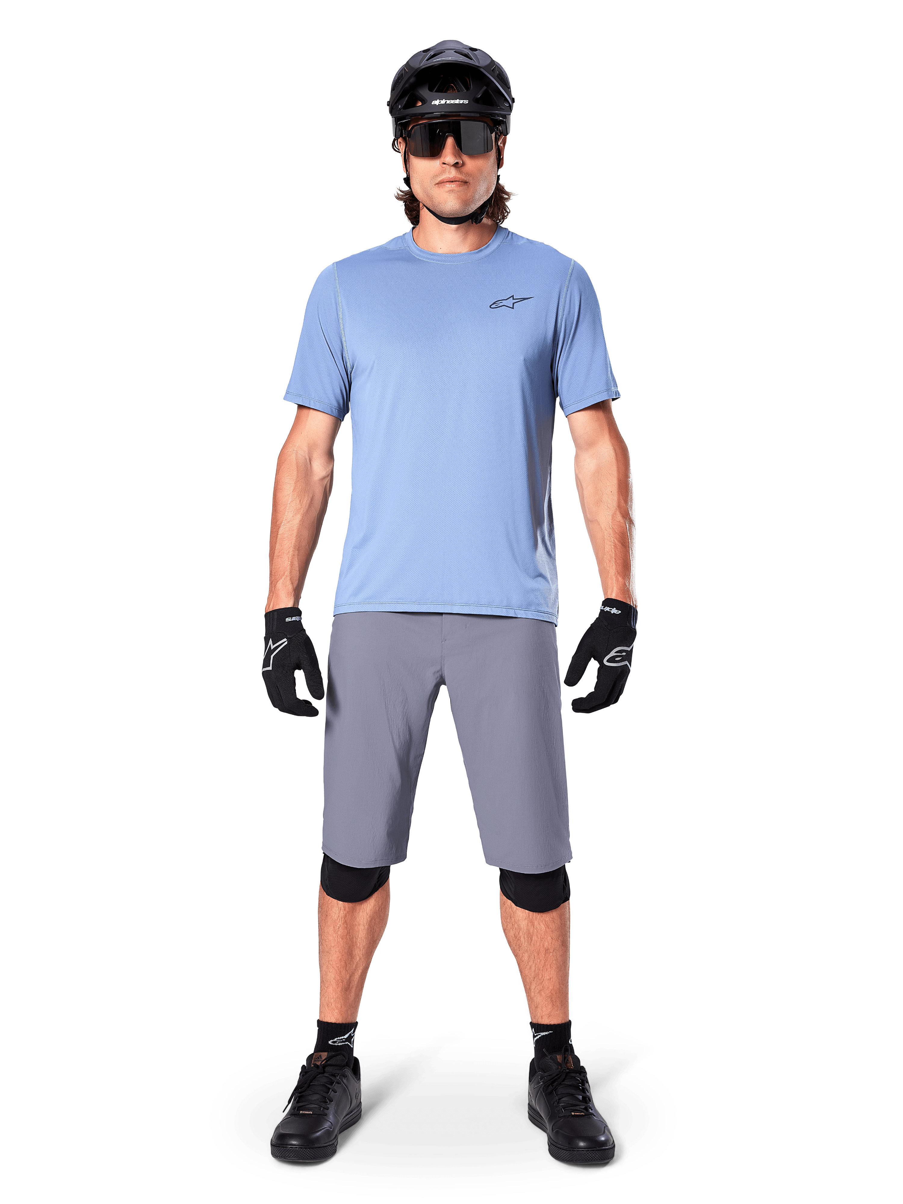 Mandlig rytter iført Alpinestars A-Dura Shorts i mørkegrå, kombineret med en lyseblå kortærmet t-shirt, sort hjelm, solbriller og sorte knæbeskyttere, komplet mountainbike-outfit til terrænkørsel