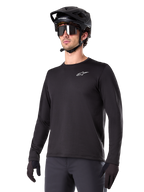Alpinestars A-Dura Thermal Jersey, sort langærmet mountainbike-trøje, hvidt logo på brystet, båret med sort hjelm og handsker, strømlinet sporty design til trailkørsel
