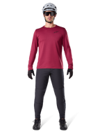 Mandlig model iført Alpinestars A-Dura Thermal Jersey i Burgundy, langærmet isoleret cykeltrøje, kombineret med mørkegrå mountainbike-bukser, hvid hjelm, sorte solbriller og sorte handsker, professionelt MTB-udstyr til koldt vejr