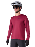 Alpinestars A-Dura Thermal Jersey, langærmet mountainbike-trøje, burgundy-rød, med isolerende fleece-for og lille sort logo på brystet, vist med grå hjelm, sorte solbriller og sorte handsker, designet til cykling i koldt vejr