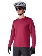 Alpinestars A-Dura Thermal Jersey, langærmet mountainbike-trøje, burgundy-rød, med isolerende fleece-for og lille sort logo på brystet, vist med grå hjelm, sorte solbriller og sorte handsker, designet til cykling i koldt vejr