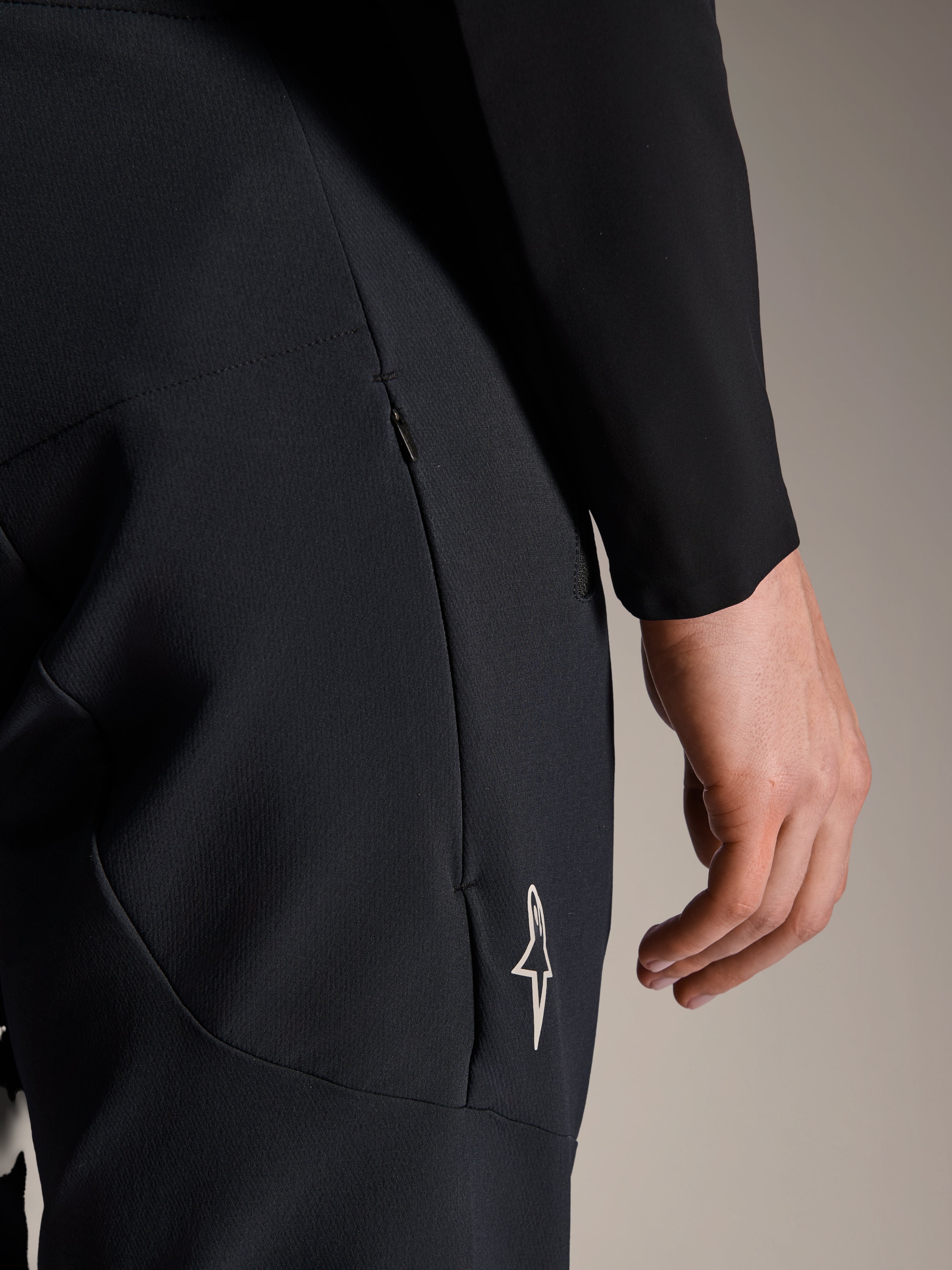 Close-up of Alpinestars A-Aria Elite Pants in Black Titanium, featuring a zippered side pocket and small white star logo, technical mountain bike pants designed for performance cycling