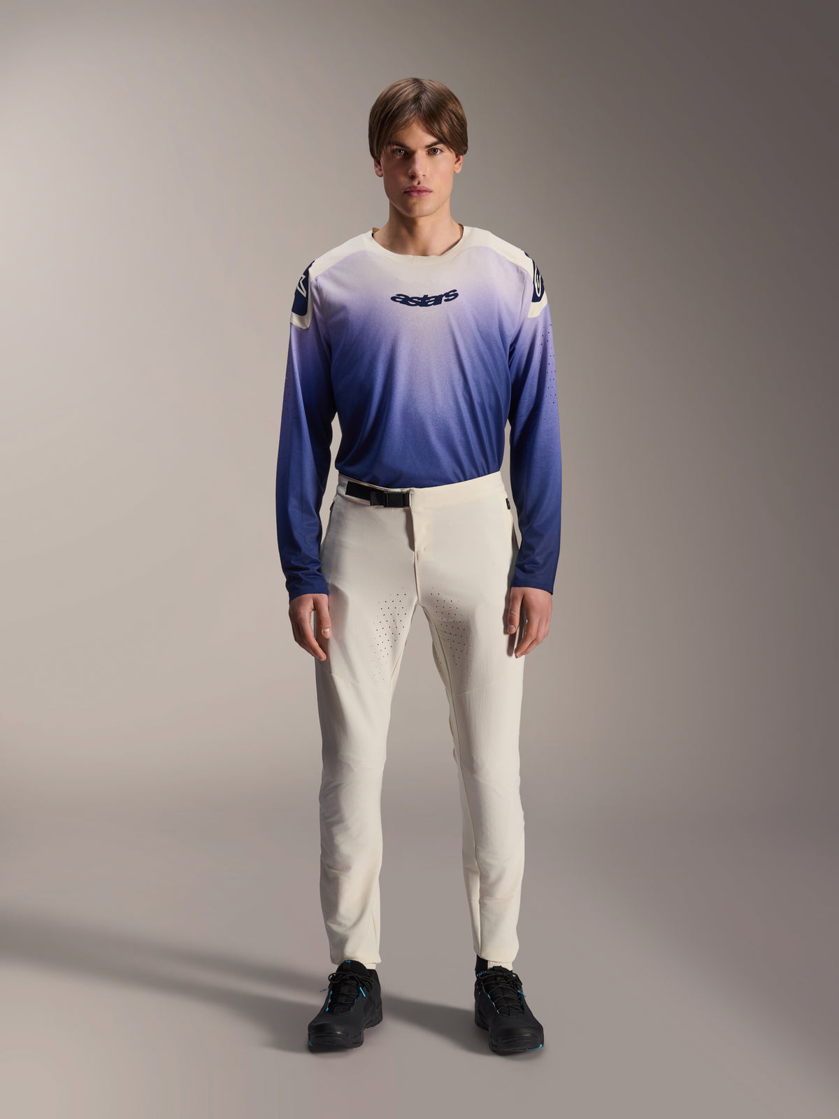 Alpinestars A-Aria Elite bukser, ecru performance MTB-bukser, råhvide cykelbukser med laserperforerede lårpaneler og magnetisk spænde, båret med blå langærmet trøje med farveovergang og sorte sko, performance-pasform til trail-kørsel