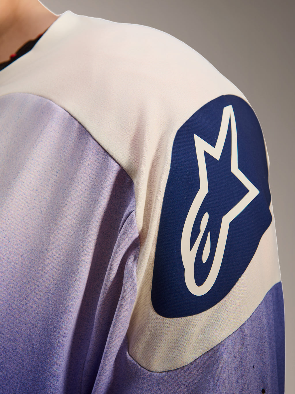 Alpinestars A-Aria Polartec Maker Elite trøje, langærmet mountainbiketrøje, Baja Blue og hvid, nærbillede af skulderen med et stort blåt cirkulært Alpinestars-logo med en hvid stjerne, viser laserperforeringer og teknisk stoftekstur