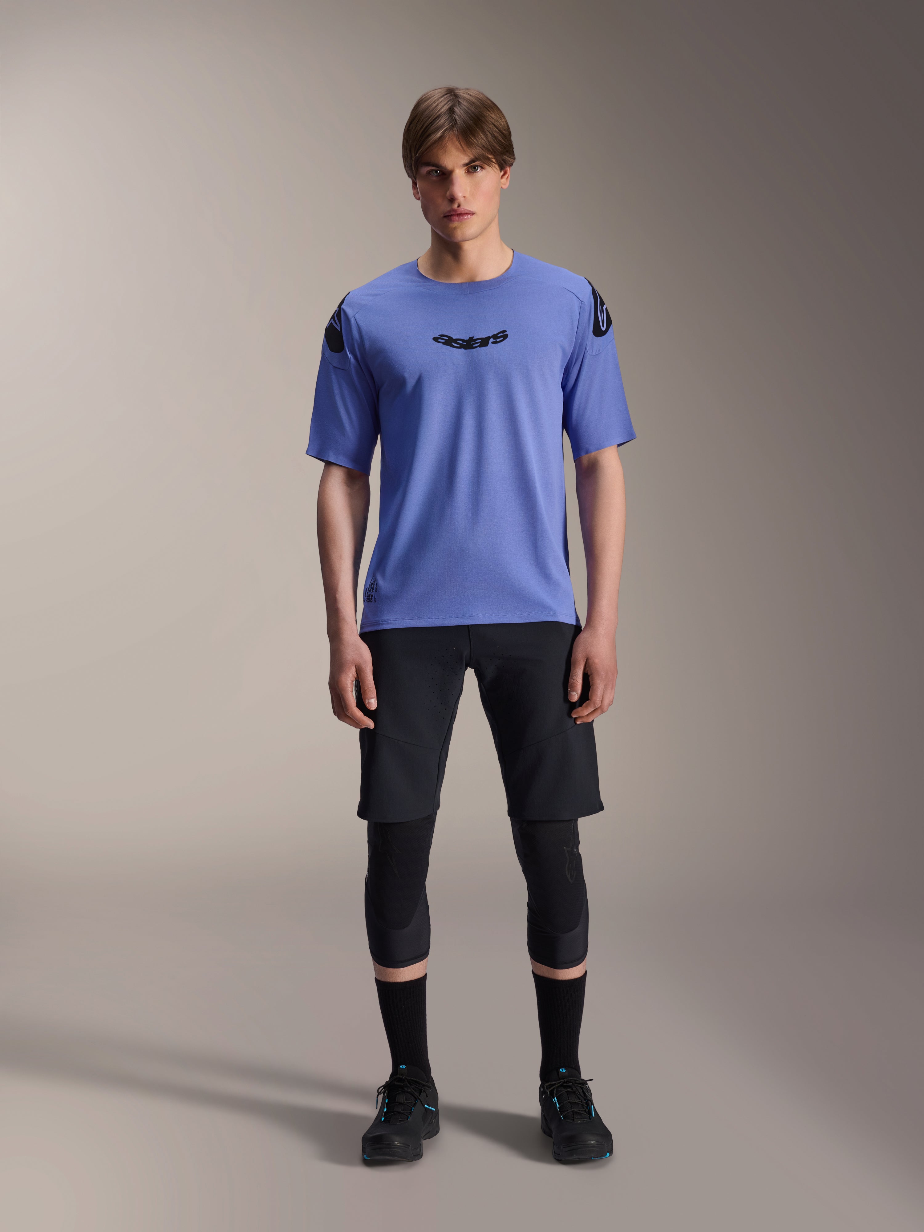 Alpinestars A-Aria Lite Short, herre mountainbike shorts, sort, båret med lys lilla kortærmet jersey og sorte knæbeskyttere, performance MTB-beklædning
