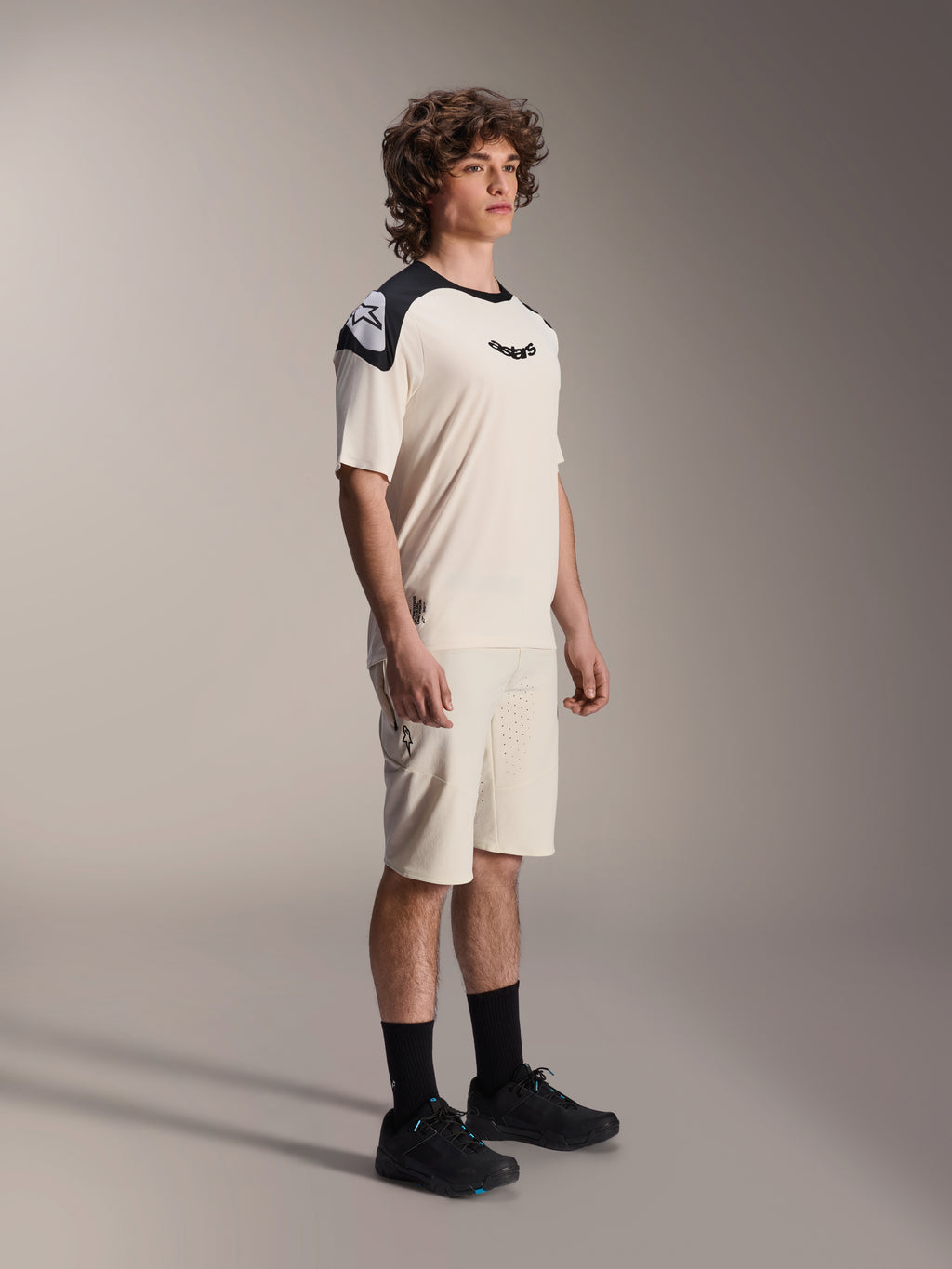Mandlig model iført Alpinestars A-Aria Elite Shorts i Ecru, tekniske mountainbike-shorts med laserskåret ventilation, parret med en matchende creme- og sort kortærmet trøje og sorte sko, professionel cykelbeklædning