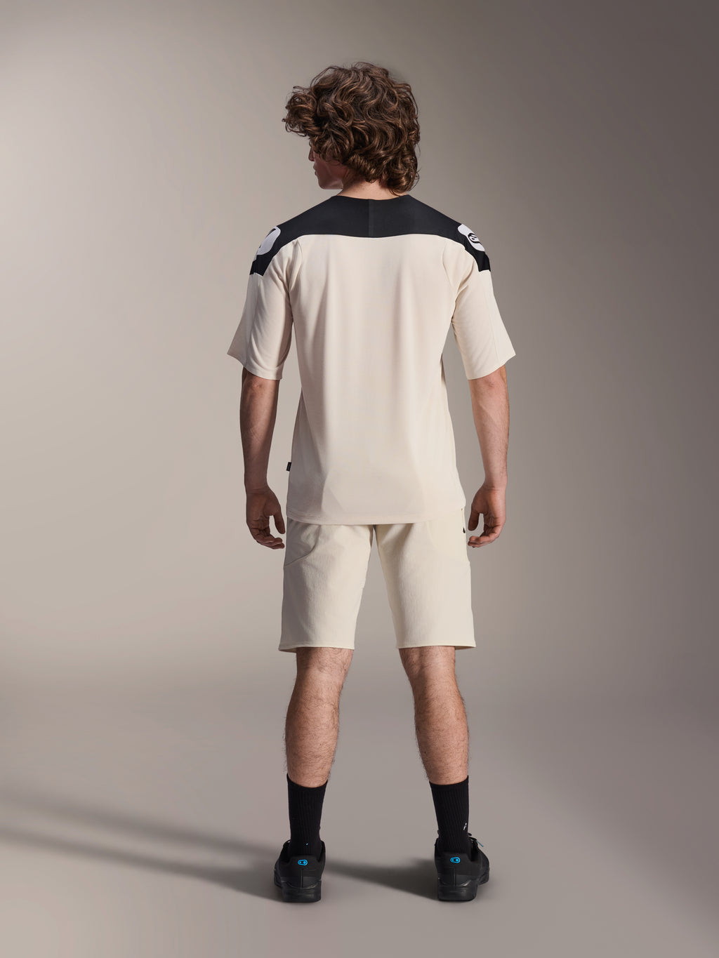 Alpinestars A-Aria Elite Shorts og A-Aria Polartec Elite SS Jersey, Ecru med sorte skulderpaneler, model set bagfra i mountainbike-udstyr, stylet med sorte strømper og sko