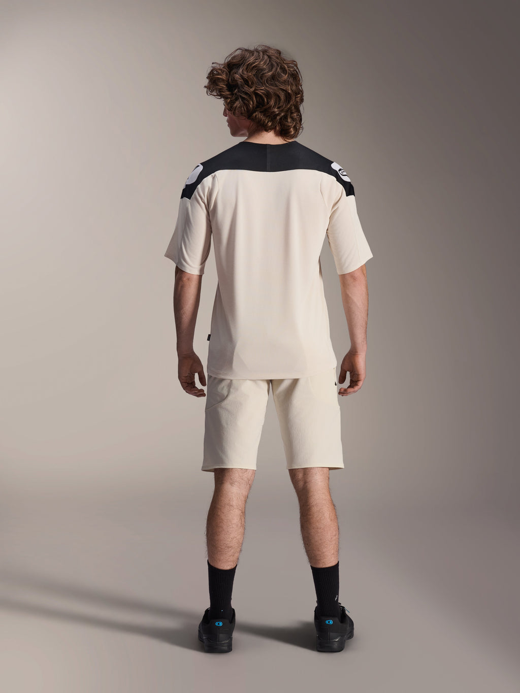 Alpinestars A-Aria Polartec Elite kortærmet jersey, MTB-cykeltrøje, Ecru med sorte skulderpaneler, set bagfra med matchende shorts og sorte strømper, ydeevnepasform med drop tail-design til terrænkørsel