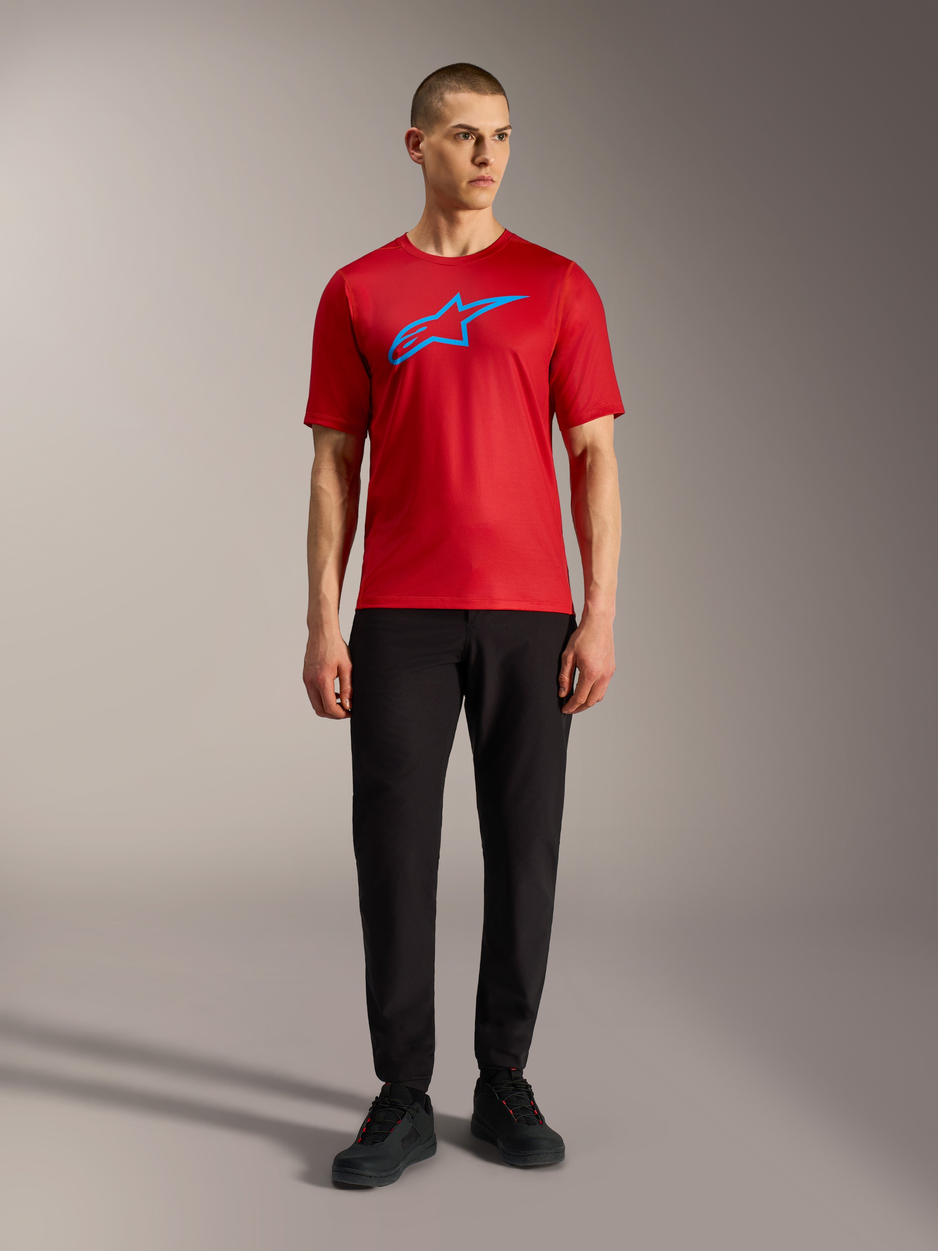 Rød Alpinestars A-Dura Ride kortærmet trøje med blåt logo, stylet med sorte bukser for et afslappet MTB-look.
