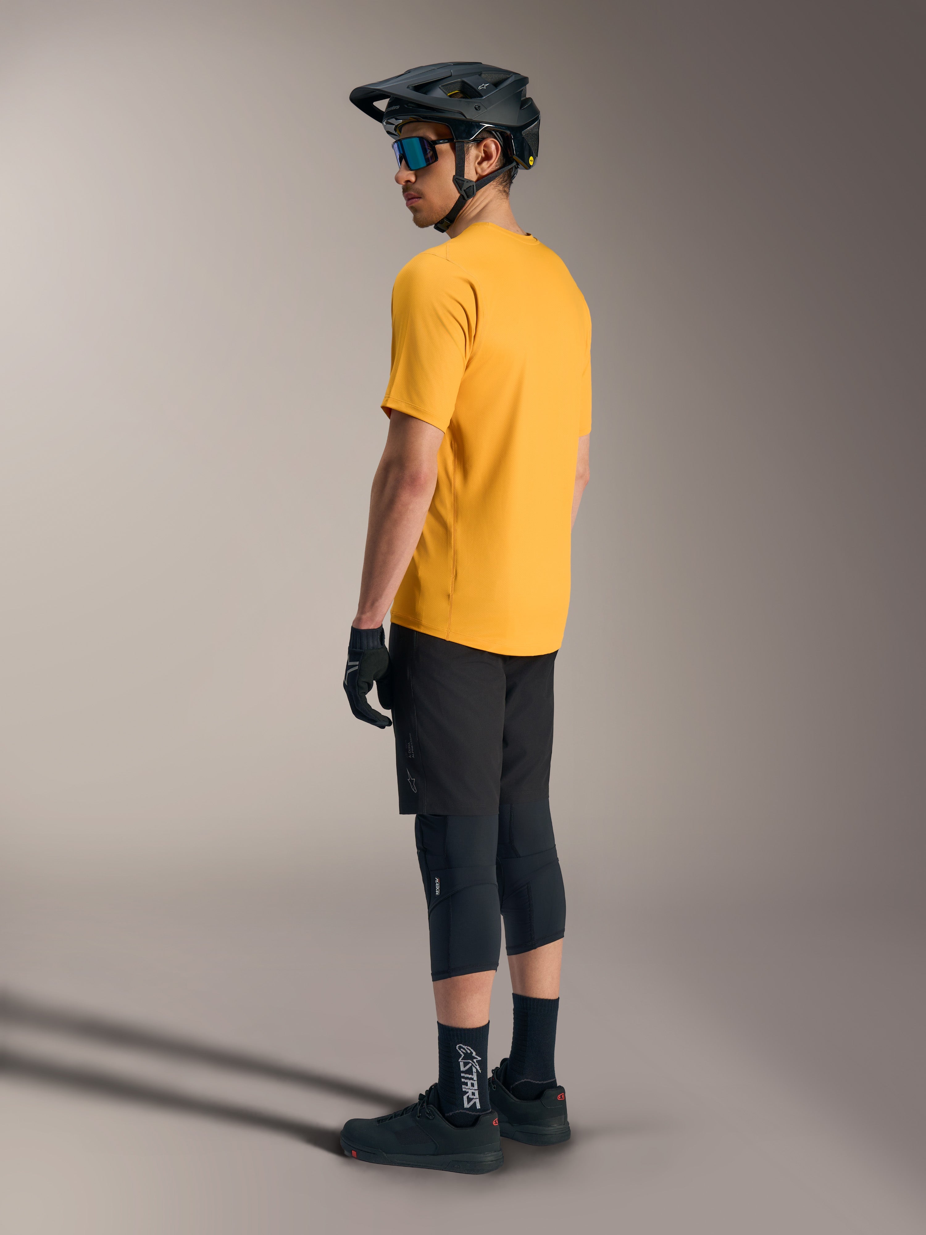 Alpinestars A-Dura Ride kortærmet trøje i orange, set bagfra på rytter med sort MTB-udstyr og hjelm.