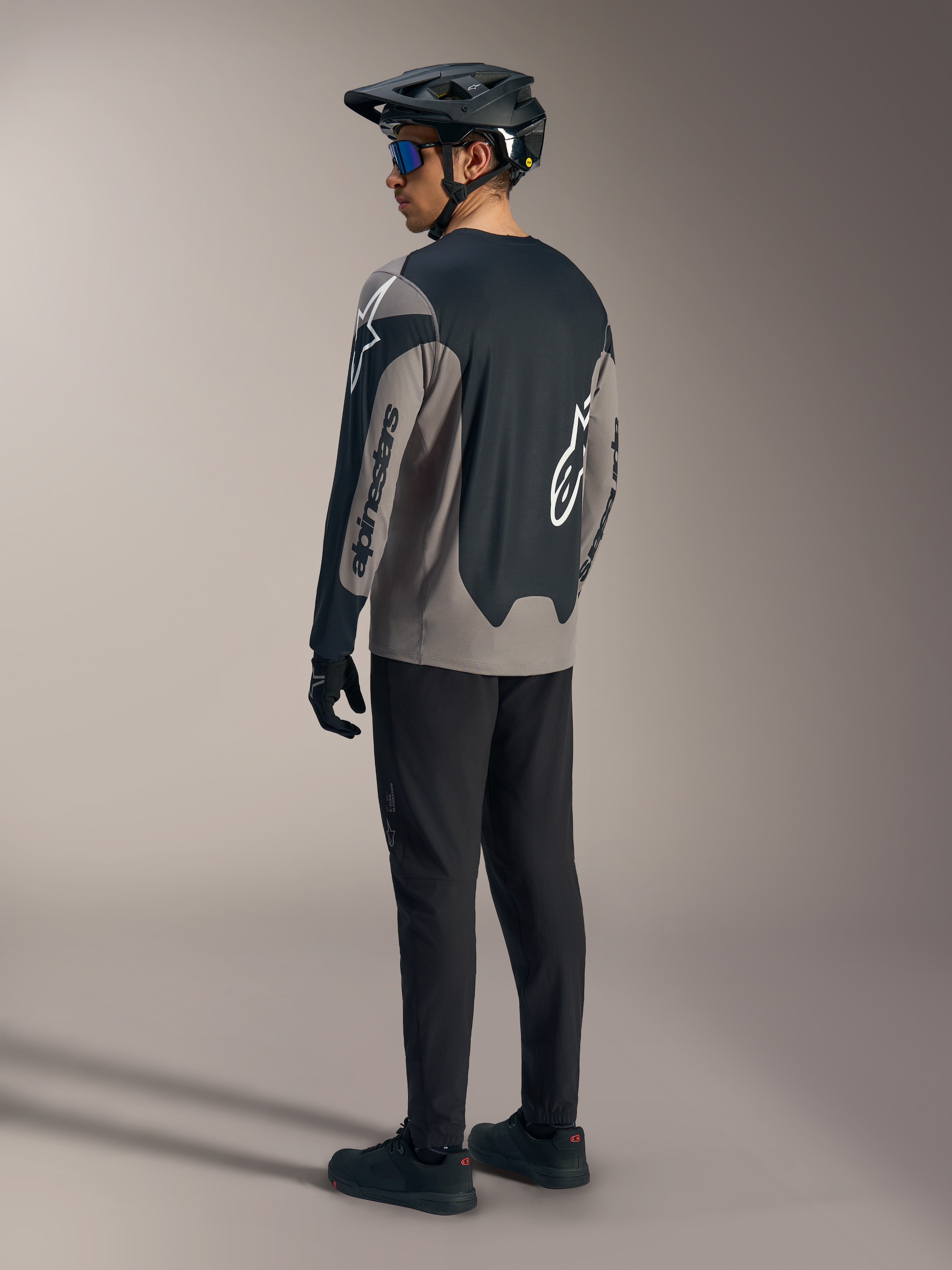 Grå og sort A-Dura Race langærmet trøje med Alpinestars-branding, vist bagfra i et komplet MTB-sæt.
