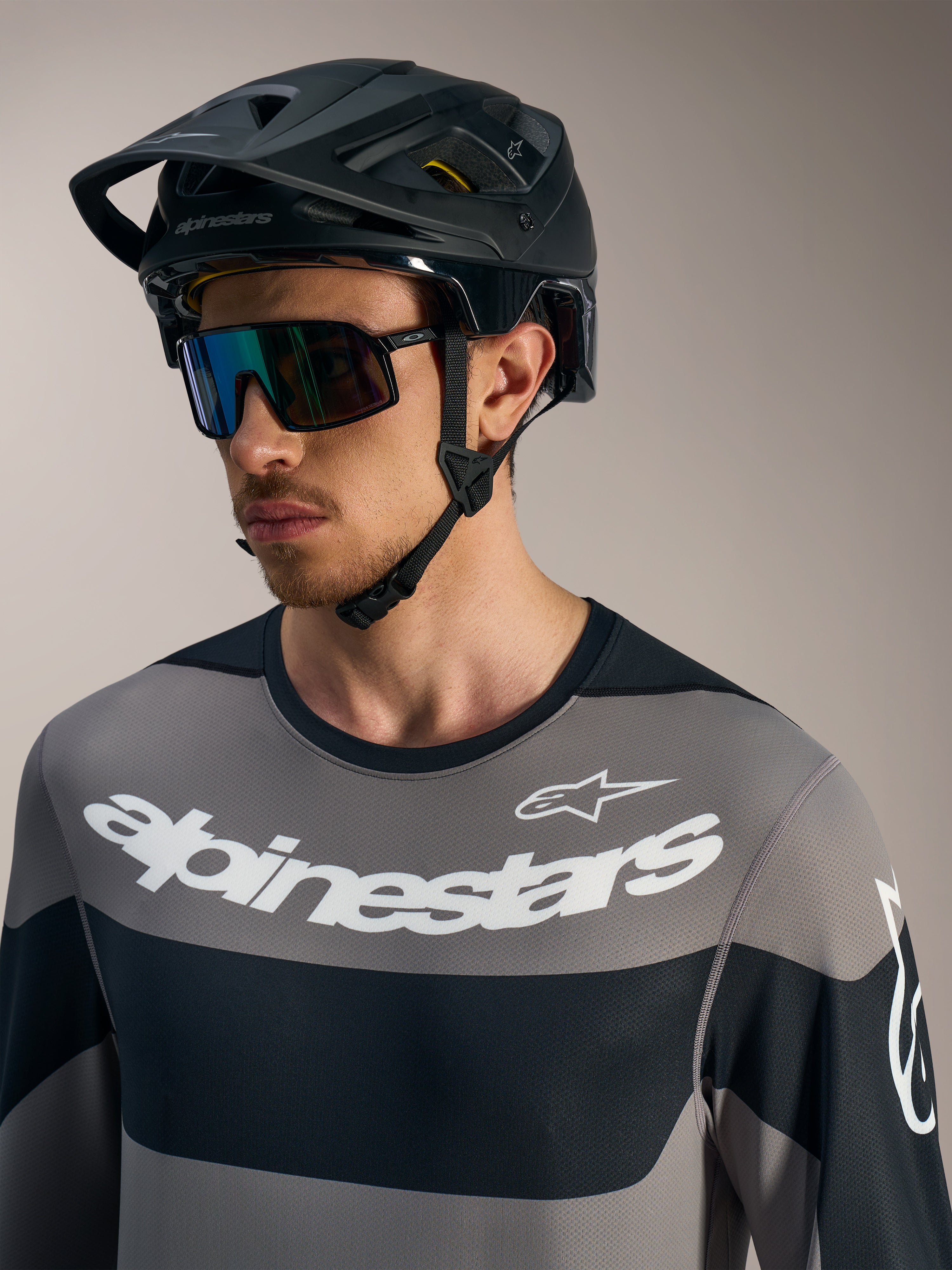 Alpinestars A-Dura Race trøje, langærmet grå med hvide logoer, sort MTB-hjelm og performance-solbriller.