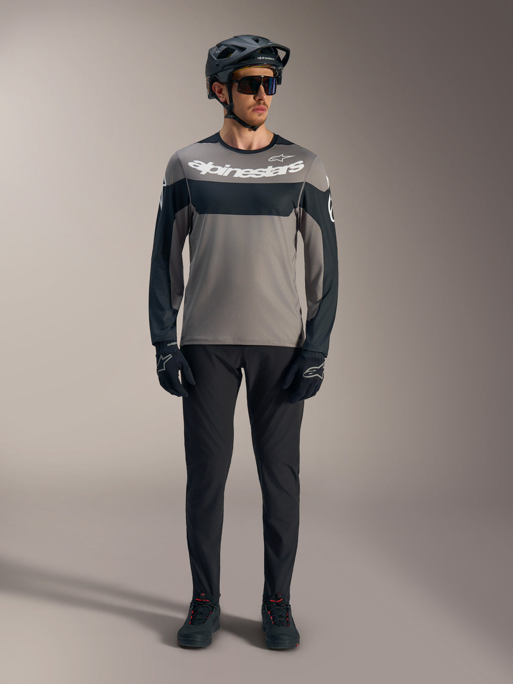A-Dura Race langærmet trøje i grå og sort med hvidt Alpinestars-logo, stylet med teknisk MTB-udstyr.