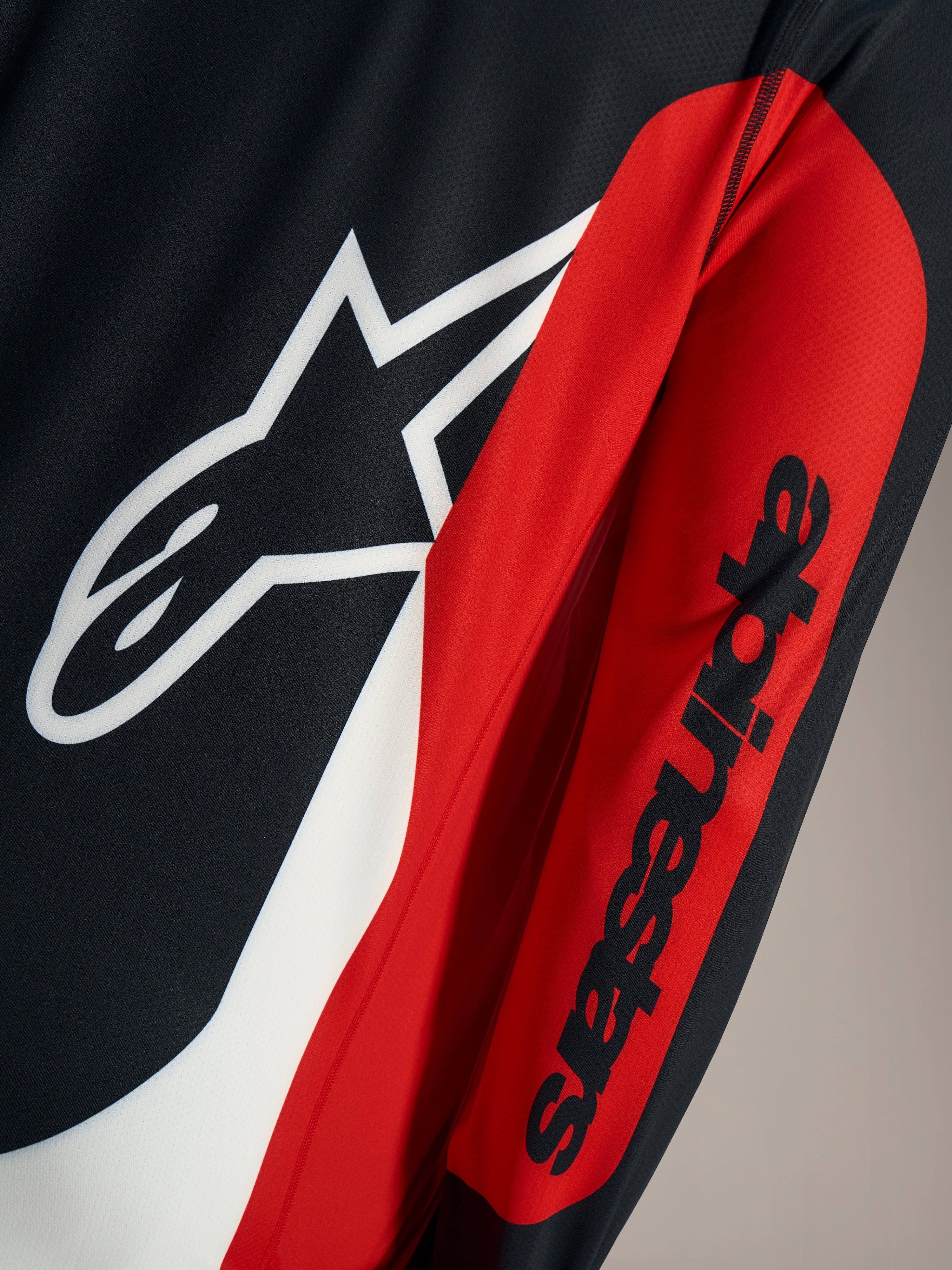 A-Dura Race Trøje detalje med hvidt Astars-logo og sort ordmærke på rødt og sort teknisk mesh-stof.
