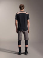 Alpinestars A-Dura Lipan Jersey - Kortærmet, sort med lysebrunt øvre rygpanel, set bagfra med forlænget rygstykke, båret med grå MTB-shorts og sorte knæbeskyttere, performance mountainbike-beklædning