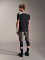 Alpinestars A-Dura Lipan kortærmet jersey i sort, set bagfra på model, der viser det lysebrune perforerede mesh-panel over den øverste del af ryggen, kombineret med grå mountainbike-shorts og sorte knæbeskyttere for et komplet trail-outfit.