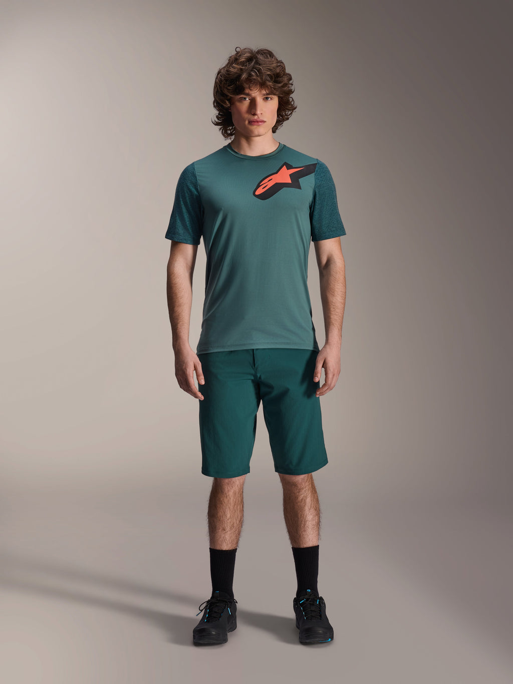 Alpinestars A-Dura Lipan trøje, kortærmet MTB-trøje, Silver Pine grøn med sort og orange Astars-logo på brystet, kombineret med matchende shorts og sort fodtøj, teknisk mountainbike-beklædning
