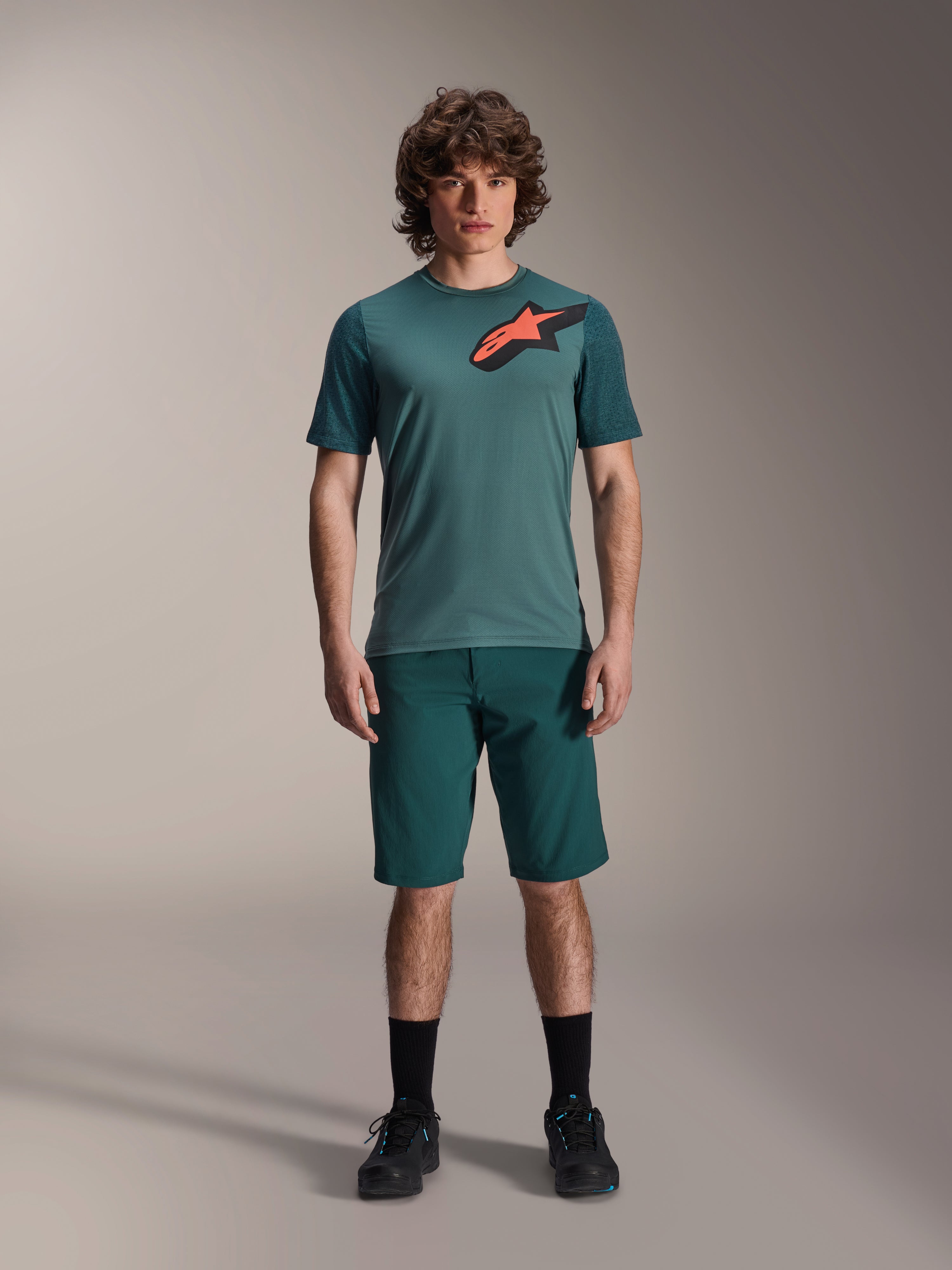 Alpinestars A-Dura Lipan trøje, kortærmet MTB-trøje, Silver Pine grøn med sort og orange Astars-logo på brystet, kombineret med matchende shorts og sort fodtøj, teknisk mountainbike-beklædning