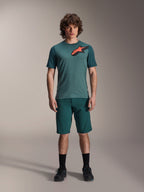 Alpinestars A-Dura Shorts i Dark Pine, mountainbikeshorts til mænd, vist på en model med en matchende blågrøn kortærmet jersey med rødt og sort stjernelogo, sorte sokker og cykelsko, afslappet sportsligt mountainbike-tøj