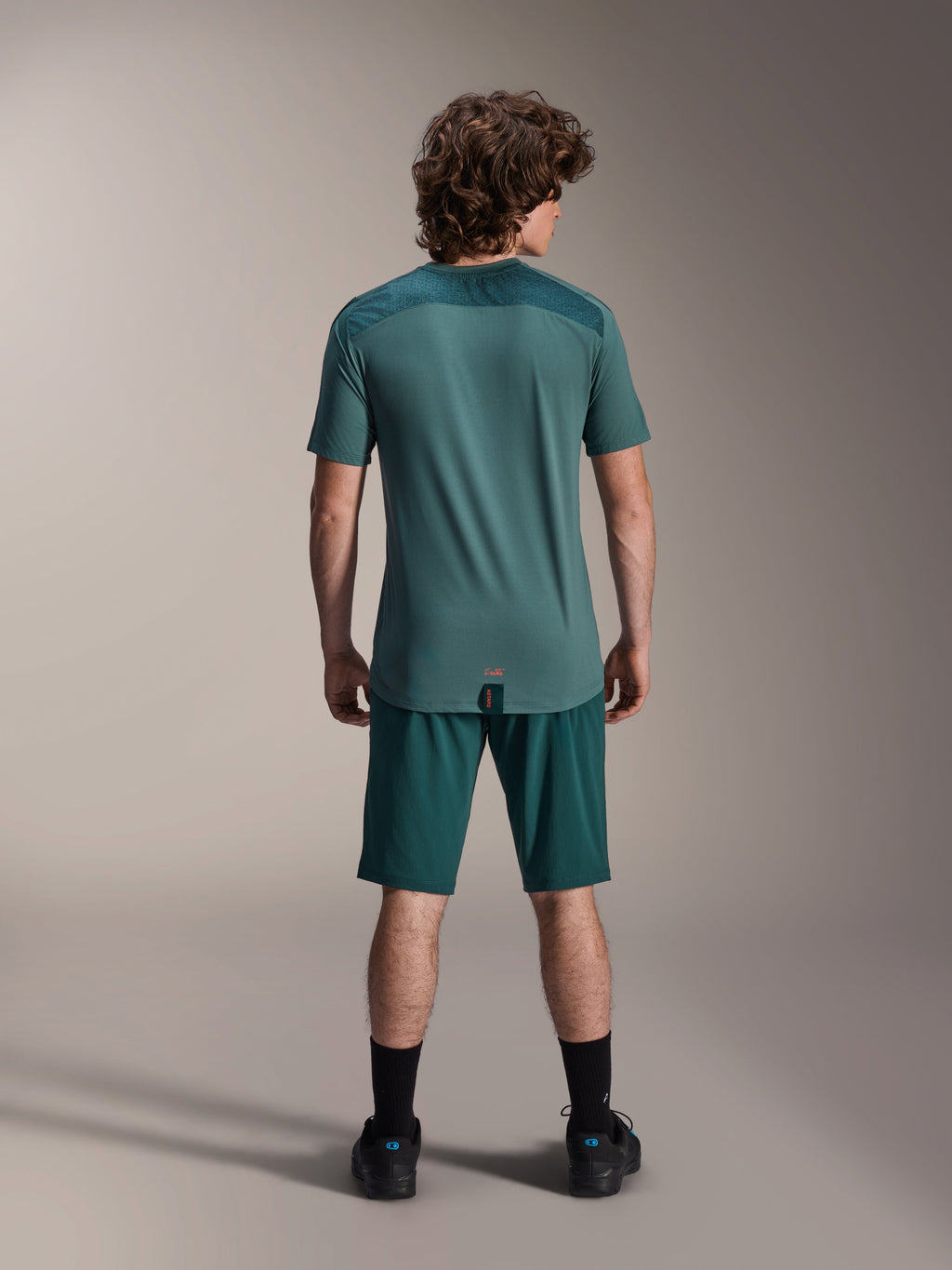 Alpinestars A-Dura Lipan kortærmet jersey i Silver Pine, set bagfra, der viser de teksturerede jacquard-skulderpaneler og drop tail-kant, båret med matchende mørkegrønne mountainbike-shorts og sort fodtøj.