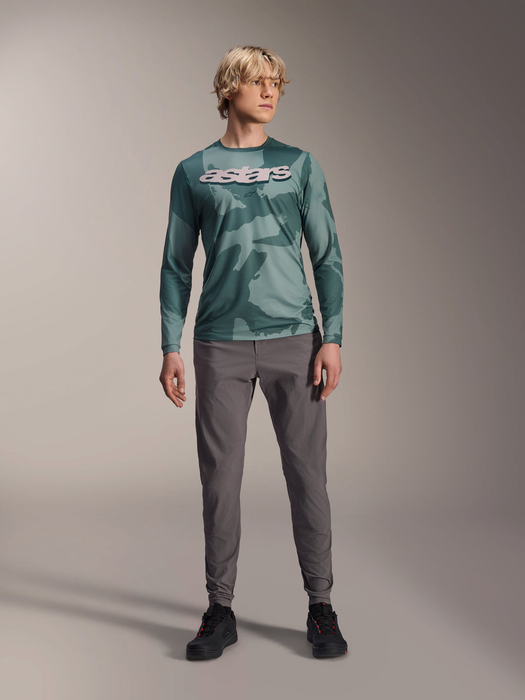 Alpinestars A-Dura Hollow Camo langærmet trøje, Silver Pine Camo med grønt camouflagemønster, stort hvidt "astars"-logo på brystet, båret med grå tekniske bukser og sorte cykelsko, højtydende MTB-udstyr