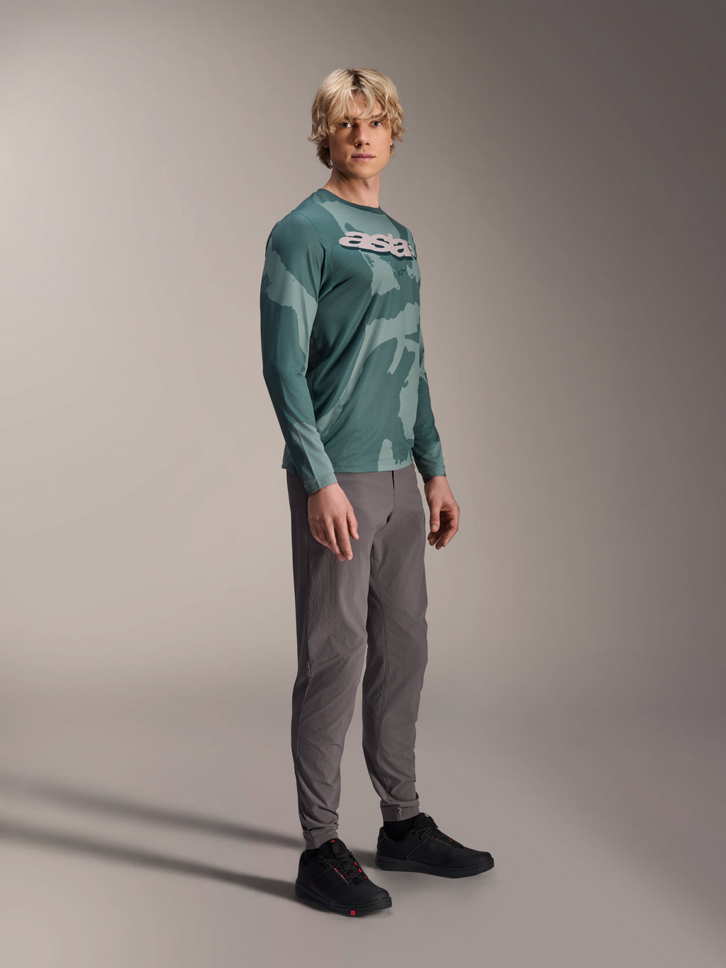 Alpinestars A-Dura Hollow Camo langærmet trøje, Silver Pine Camo, båret af en model med grå bukser og sorte sko, med grønt camouflagemønster og et markant hvidt ASTARS-logo på brystet, højtydende MTB-beklædning
