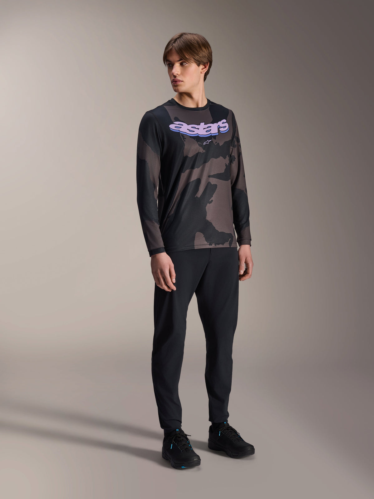 Alpinestars A-Dura Hollow Camo langærmet trøje, sort camouflagemønster med lilla 'astars' grafik på brystet, kombineret med sorte tekniske bukser og sorte sko, afslappet MTB-udstyr