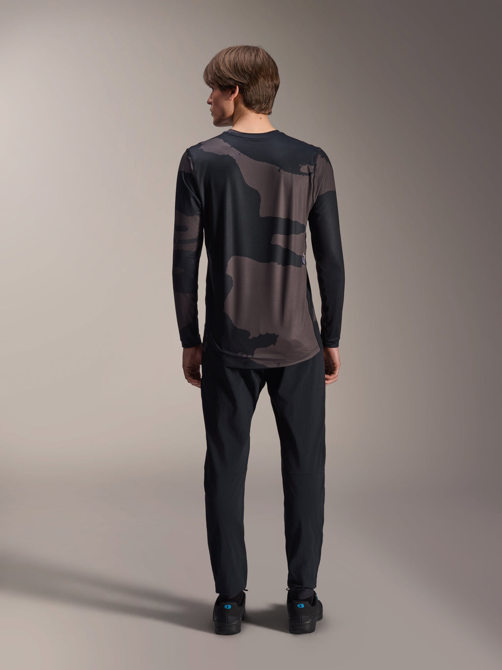 Alpinestars A-Dura Hollow Camo langærmet trøje, Black Camo, set bagfra båret med sorte bukser, med et mørkt camouflage-mønster og forlænget bagkant for MTB-dækning.