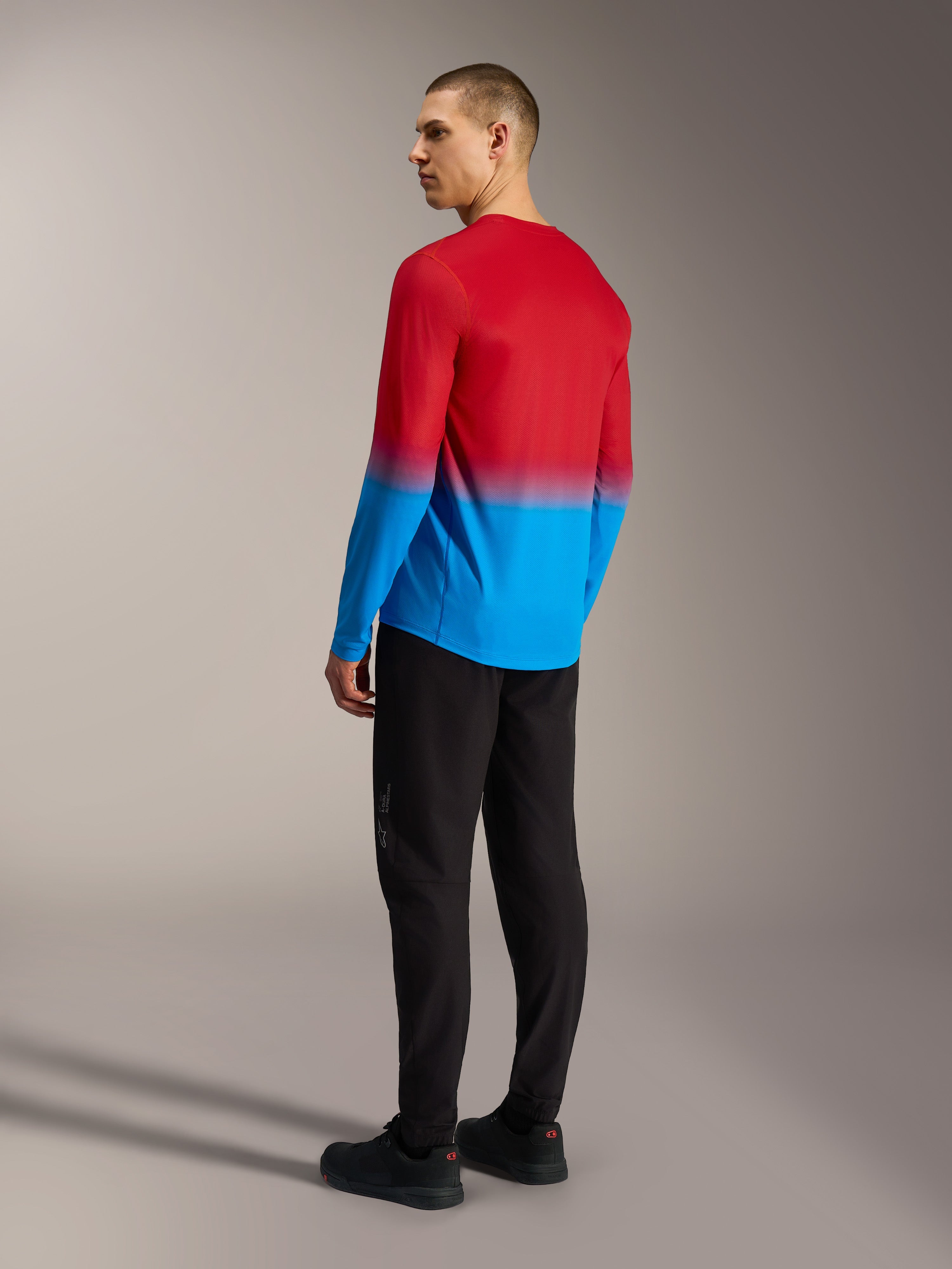 Alpinestars A-Dura ASTARS 2.0 langærmet MTB-jersey i rød og blå gradient, set bagfra på model i sorte bukser.