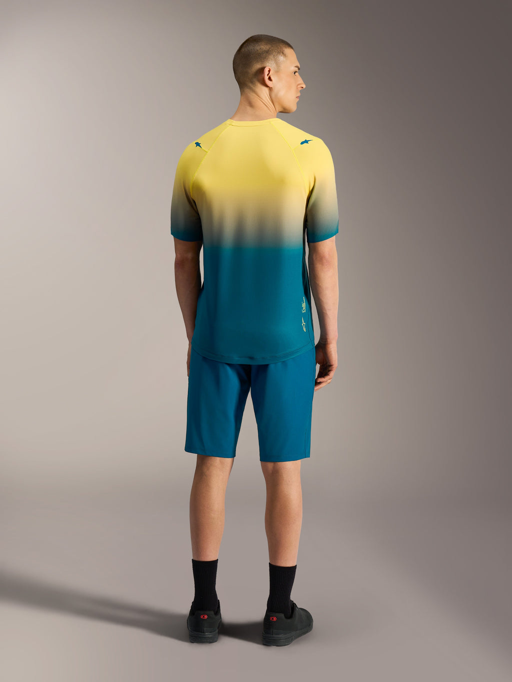 A-Dura ASTARS Jersey 2.0, kortærmet MTB-trøje med gul og blågrøn gradient, vist bagfra på en model.