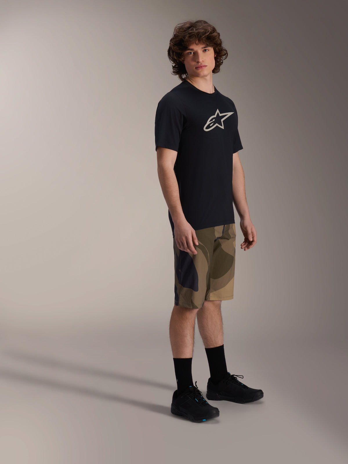 Alpinestars A-Dura Astar kortærmet trøje, sort med hvidt brystlogo, båret med camouflage-shorts og sorte MTB-sko, afslappet mountainbike-udstyr