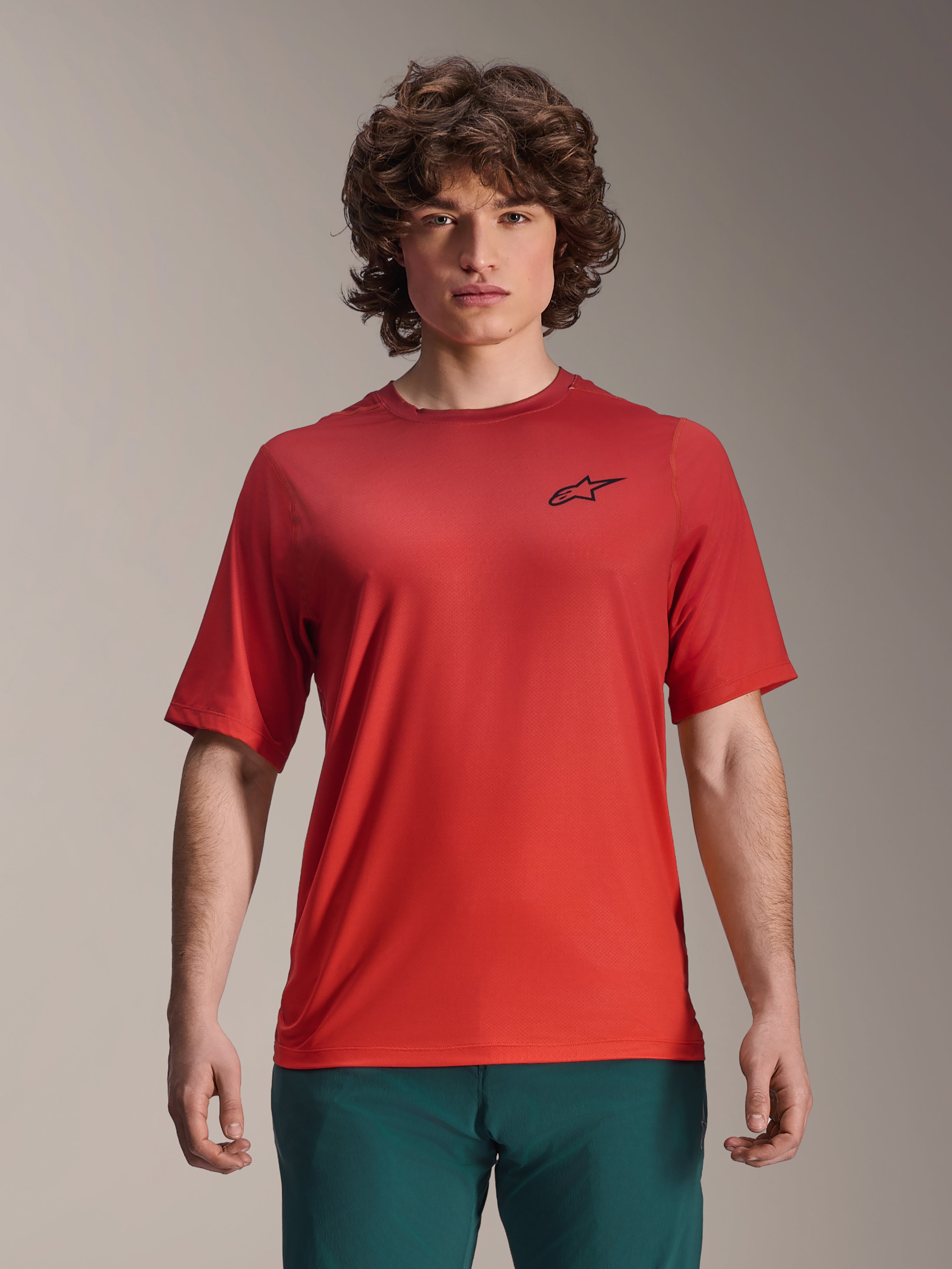 Alpinestars 2025 A-Dura Rise trøje, kortærmet MTB-trøje, Spicy Orange, båret af en mand, med et sort Astars-logo på brystet, kombineret med mørkegrønne bukser, afslappet mountainbike-performance-beklædning