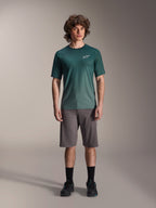 Mandlig model i Alpinestars A-Dura Rise Jersey - Kortærmet i Silver Pine, grøn cykeltrøje med lille hvidt logo på brystet, kombineret med grå mountainbike-shorts og sort fodtøj, afslappet MTB-trailudstyr
