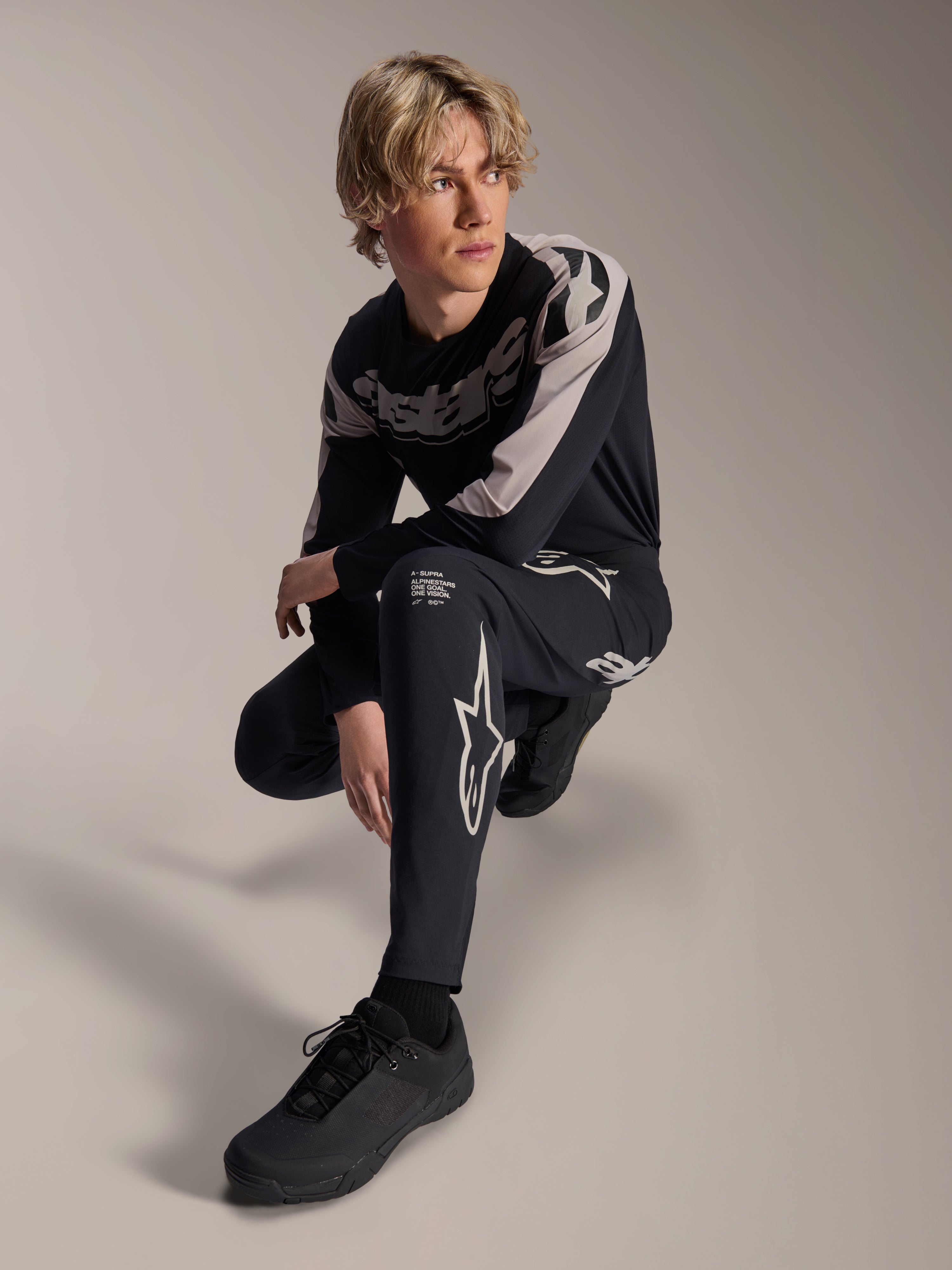 Alpinestars A-Supra Melt Pants and Long Sleeve Jersey, Black and Grey, featuring bold white branding and star logos, worn by a male model in a crouching pose, coordinated MTB racing gear
