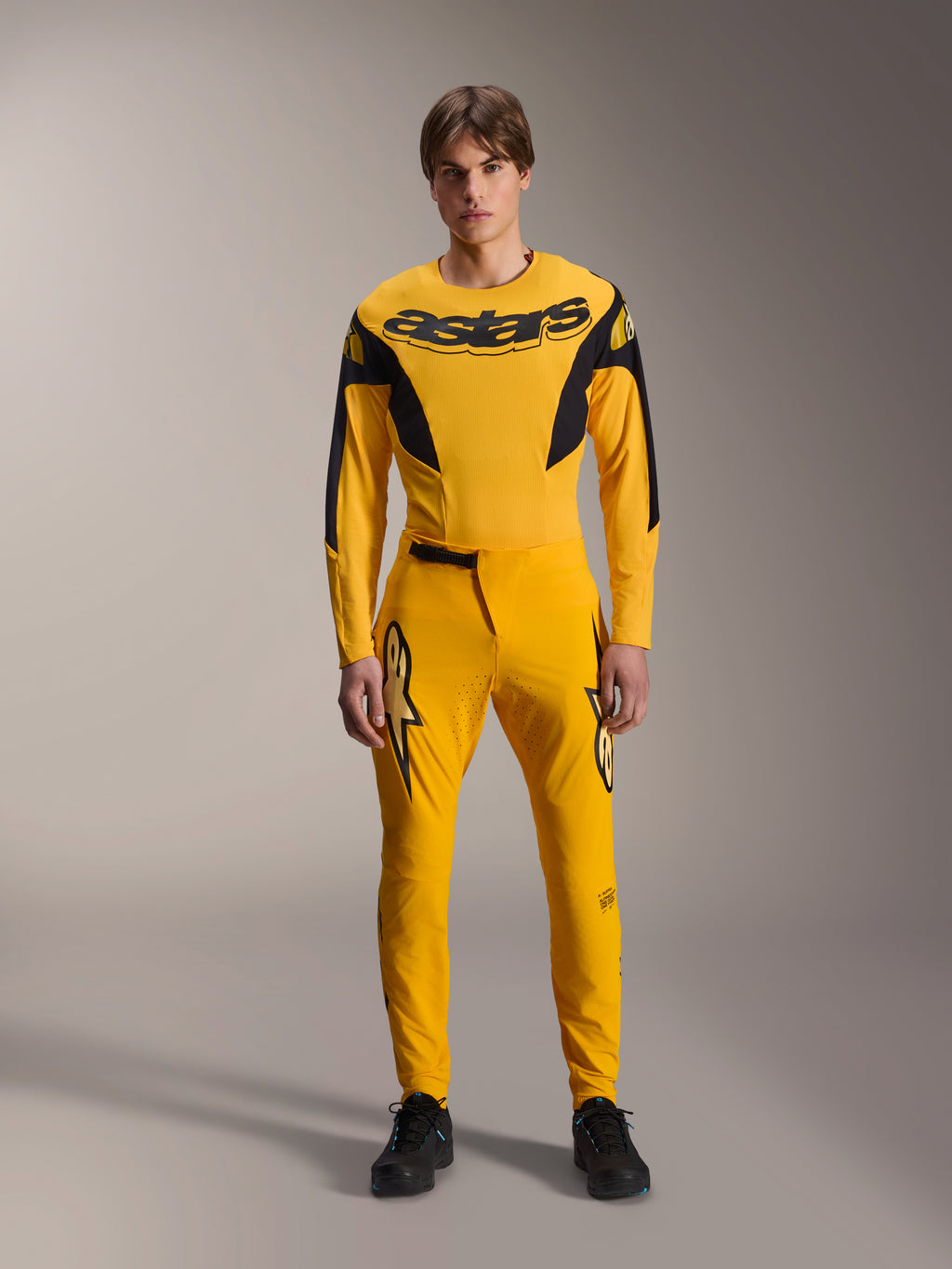 Limited Edition A-Supra Melt Gold udstyrssæt, Alpinestars mountainbike-beklædning, mørkegul og sort, model iført langærmet trøje med markant 'astars' brystlogo og matchende performance-bukser, med laserskåret ventilation på inderlårene og en sikker skraldelukning i taljen, professionelt MTB-racersæt