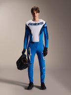 Mandlig model iført Alpinestars A-Supra Melt MTB-sæt, hvid og blå langærmet trøje med 'astars' ordmærke, blå A-Supra Melt bukser med hvidt logo, sort full-face hjelm, sorte handsker og sko, koordineret terræncykel-outfit