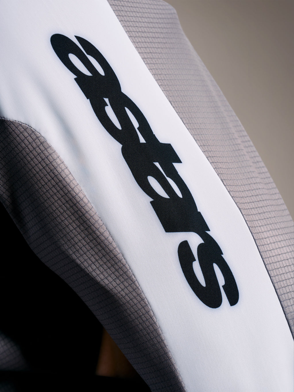 Detalje af A-Supra Elite-trøjen, gråt mikroperforeret stof med sort ASTARS-logo på hvidt ærmebånd.