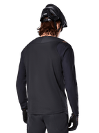 Alpinestars A-Aria Polartec Switch langærmet trøje, sort, set bagfra, båret med en sort MTB-hjelm og handsker, med drop tail-design til off-road ydeevne