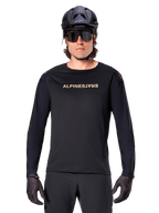 Alpinestars A-Aria Polartec Switch langærmet jersey, sort, guld Alpinestars-logo på brystet, båret med sort MTB-hjelm, mørke solbriller og sorte handsker, professionelt mountainbike-trailudstyr